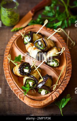 Auberginen-Rollen mit Pesto und Feta auf Vintage-Holzplatte. Weichfokus Stockfoto