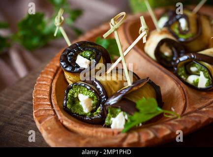 Auberginen-Rollen mit Pesto und Feta auf Vintage-Holzplatte. Weichfokus Stockfoto