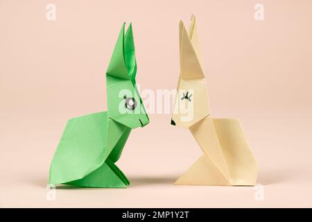Grüne und gelbe Origami-Kaninchen auf beigem Hintergrund. Basteln für Ostern, aus Papier falten, selbst machen Stockfoto