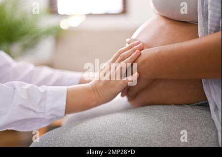 Seitenansicht eines Arztes, der den Bauch einer schwangeren Frau berührt und das Baby im Bauch spürt. Medizinisches Schwangerschaftscheckkonzept Stockfoto