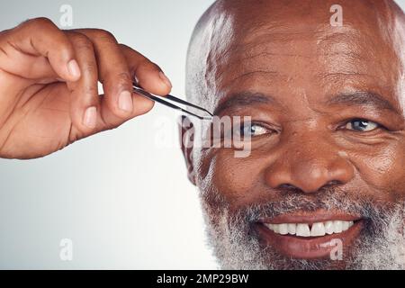Pflege, Lächeln und schwarzer Mann mit Pinzette zur Haarentfernung isoliert auf grauem Studiohintergrund. Reinigungs-, Routine- und hochrangige afrikanische Person mit einem Stockfoto