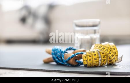 Ein Seil, ein Maßband und ein Glas Wasser auf einer Matte zu Hause im Wohnzimmer. Konzept einer gesunden Lebensweise. Stockfoto