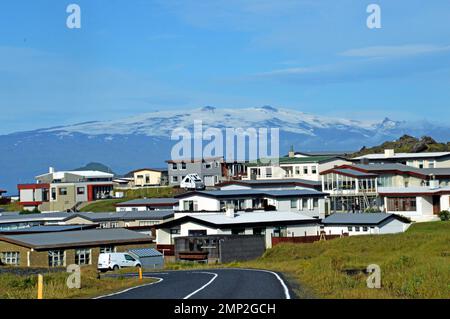 Island, Insel Heimaey: Moderne Häuser in der Oberstadt, mit dem schneebedeckten Massiv Mýrdalsjökull auf dem Festland als Hintergrund. Stockfoto