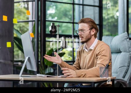 Frustrierter und verärgerter Geschäftsmann, der online Nachrichten auf dem Computermonitor liest, junger blonder Mann, der im Büro in lässiger Kleidung traurig ist und mit den Ergebnissen nicht zufrieden ist. Stockfoto