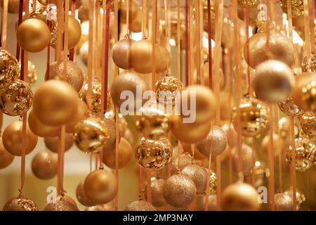 Goldene Weihnachtskugeln hängen über dem Band saisonale Weihnachtsfeier mit weichem Fokus, tropfenförmiger Fokus, ätherische magische Partydekoration Stockfoto