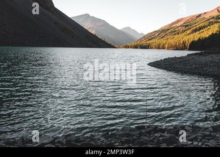 Eine Angelrute liegt im Schatten auf den Felsen des alpinen Sees Shavlinskoe. Stockfoto