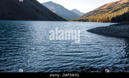 Eine Angelrute liegt im Schatten auf den Felsen am Ufer des alpinen Sees Shavlinskoye. Stockfoto