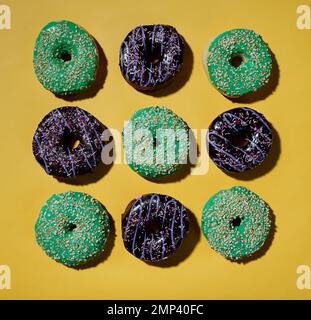 Mehrfarbiges Donuts-Muster auf gelbem Hintergrund. Harte Schatten. Flach verlegt. Draufsicht Stockfoto