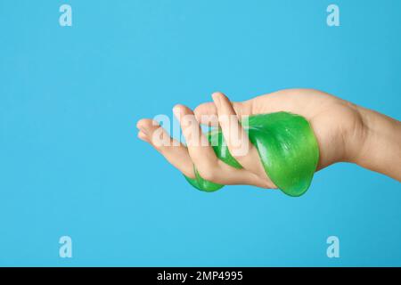 Frau spielt mit grünem Schleim auf hellblauem Hintergrund, Nahaufnahme. Anti-Stress-Spielzeug Stockfoto