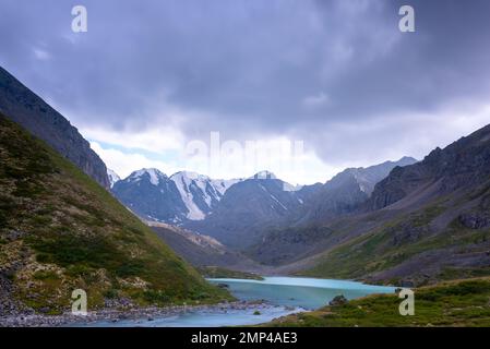 Bergsee ruhiges Türkis mit klarem Wasser Karakabak im Altai-Gebirge mit Schnee und Gletschern unter dicken Wolken. Stockfoto