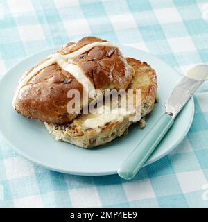 Heiße Kreuzbrötchen gebuttert in Scheiben geröstete ostern traditionelle Gingham Tischtuch Küchenmesser Butterschmelze köstlicher saisonaler Weizenboden gebackener Kuchen Stockfoto