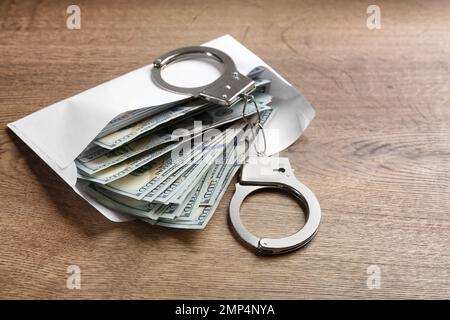 Dollarscheine und Handschellen auf Holztisch. Bestechungskonzept Stockfoto