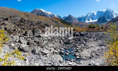 Trockener Boden ohne Wasser, ein See mit Steinen und ein kleiner Bach in den Bergen vor dem Hintergrund von schneebedeckten Gipfeln mit Gletschern in Altai während der Zeit Stockfoto