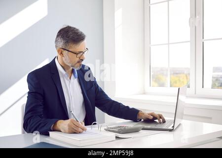 Ein fokussierter Geschäftsmann berechnet die Ausgaben am Arbeitsplatz und bezahlt Rechnungen und Steuern online. Stockfoto