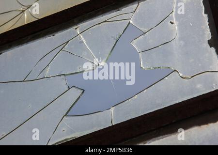 Zerbrochenes Glas im Fenster. Hintergrundhimmel, Gefahr, Verwüstung Stockfoto