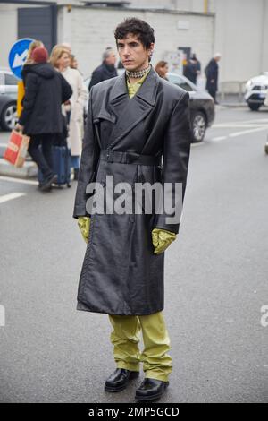 MAILAND, ITALIEN - 15. JANUAR 2023: Mann mit schwarzem Ledermantel und säuregrüner Hose vor der Prada-Modenschau, Mailand Fashion Week Street Style Stockfoto