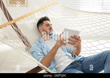 Junger Mann liest zu Hause Buch in der Hängematte Stockfoto