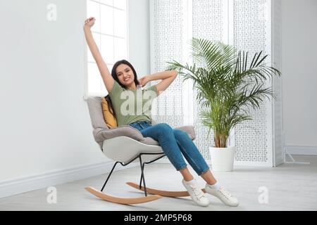 Junge Frau, die sich zu Hause im Schaukelstuhl entspannt Stockfoto