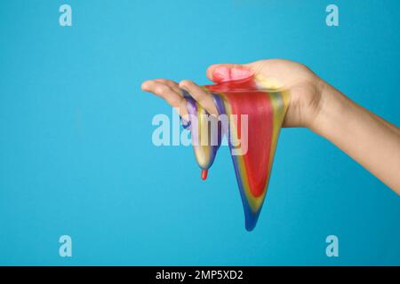 Frau spielt mit farbenfrohem Schleim auf hellblauem Hintergrund, Nahaufnahme. Anti-Stress-Spielzeug Stockfoto
