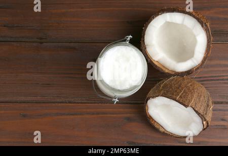 Hälften reifer Kokosnüsse und Bio-Öl auf Holztisch, flach liegend mit Platz für Text. Gesundes Kochen Stockfoto