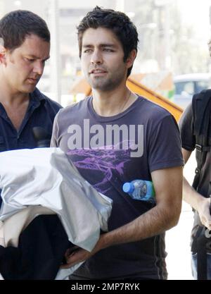 Der „Enourage“-Schauspieler Adrian Grenier geht mit einem Mann in einem Feueranzug spazieren und sieht sich einige Bilder auf einer Digitalkamera an, während er unterwegs auf den Straßen von Los Angeles dreht. Grenier, der kürzlich bei Tagesterminen mit dem Reality-TV-Star Kim Kardashian gesehen wurde, hat sich angeblich für einen Gastauftritt in der Teenager-Drama-Serie „90210“ angemeldet. Los Angeles, Kalifornien. 08/16/10. Stockfoto