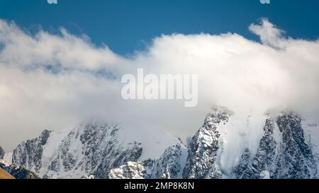 Panoramablick auf die Gipfel der Steinberge mit Gletscherzungen und Schnee bedeckt mit weißen Wolken und Nebel in Altai. Stockfoto