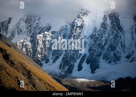 Die Gipfel der steinernen Berge mit Gletscherzungen und Schnee sind in Altai mit weißen Wolken und Nebel bedeckt vor dem Hintergrund eines Felsens. Stockfoto