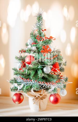 Kleiner Weihnachtsbaum mit roter Kugel und silbernen Ornamenten. Lichteffekte an der Wand Stockfoto