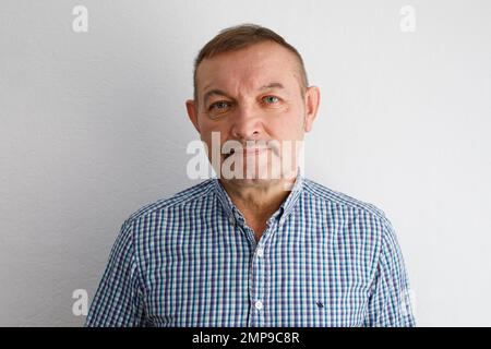 Nahaufnahme Porträt, älterer Mann in blauem Hemd, isolierter Innenbereich, weißer Hintergrund. Stockfoto