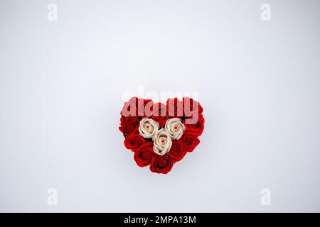 Herz aus roten und weißen Rosen auf frischer Schneeoberfläche an einem kalten Wettertag. Flach liegend, Draufsicht. Romantisches Outdoor-Konzept für den Valentinstag Stockfoto