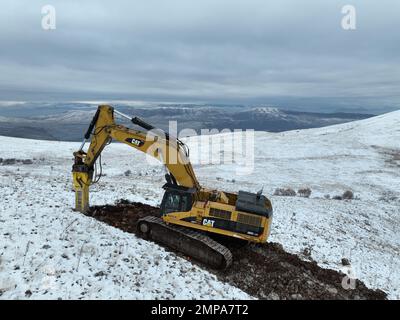 Hydraulikbagger mit hydraulischem hamme, der auf dem Berg mit Schnee und Nebel arbeitet. Stockfoto