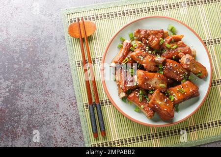 Glasierte Kurzrippchen aus Schweinefleisch in süßer und saurer Sauce in asiatischer Nahaufnahme auf einem Teller auf dem Tisch. Horizontale Draufsicht von oben Stockfoto