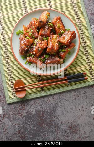 Gebratene Schweinerippchen in süßer und saurer Sauce in asiatischer Nahaufnahme auf einem Teller auf dem Tisch. Vertikale Draufsicht von oben Stockfoto