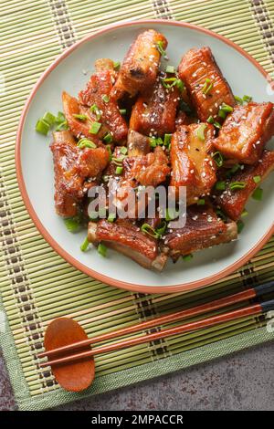 Hausgemachte chinesische Schweinerippchen in süßer und saurer Sauce in Nahaufnahme auf einem Teller auf dem Tisch. Vertikale Draufsicht von oben Stockfoto