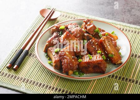 Barbecue süße und saure Rippchen mit grünen Zwiebeln und Sesam in Nahaufnahme auf einem Teller auf dem Tisch. Horizontal Stockfoto