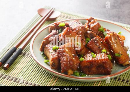 Chinesische süße und saure Rippchen mit grünen Zwiebeln und Sesam in Nahaufnahme auf einem Teller auf dem Tisch. Horizontal Stockfoto