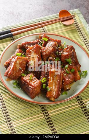 Gebratene Schweinerippchen in süßer und saurer Sauce in asiatischer Nahaufnahme auf einem Teller auf dem Tisch. Vertikal Stockfoto
