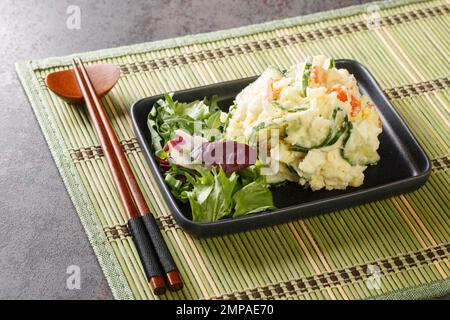 Japanischer Kartoffelsalat ist wie halb-Stampfkartoffeln gemischt mit Gemüse, Ei und Mayonnaise, Nahaufnahme auf einem Teller auf dem Tisch. Horizontal Stockfoto