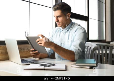 Ein Mann, der am Tisch im Café Hörbücher hört Stockfoto