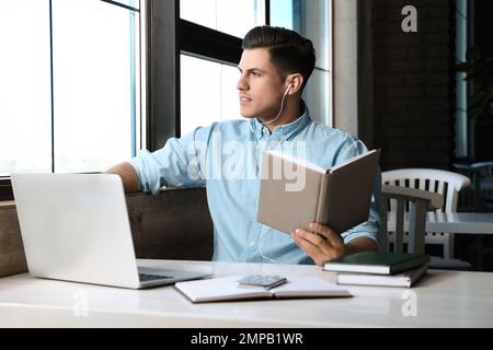 Ein Mann, der am Tisch im Café Hörbücher hört Stockfoto