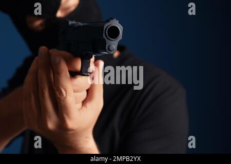 Mann mit Maske hält Waffe vor dunkelblauem Hintergrund, konzentriert euch auf die Hände Stockfoto