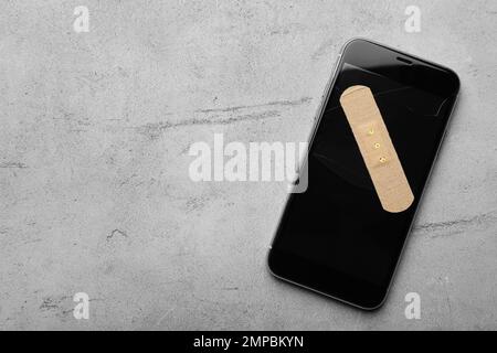 Smartphone mit aufklebendem Putz auf Tisch aus hellgrauem Stein, Draufsicht. Platz für Text Stockfoto