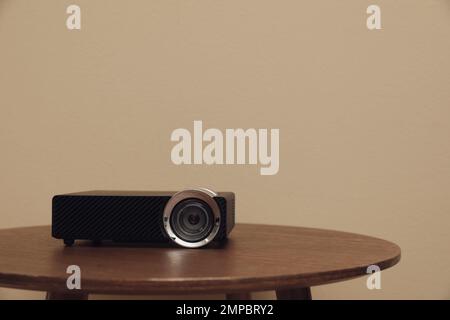 Moderner Videoprojektor auf Holztisch vor beigefarbenem Hintergrund. Platz für Text Stockfoto