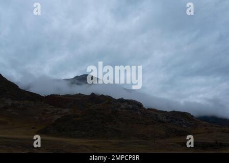 Dichter Nebel geht entlang des Berges hinab und lässt Schnee nach sich in Altai am Abend im Herbst auf dem Gipfel. Stockfoto