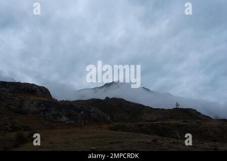 Dichter Nebel geht den Berg entlang hinunter und lässt am Abend Schnee auf dem Gipfel nach sich selbst in Altai zurück. Stockfoto