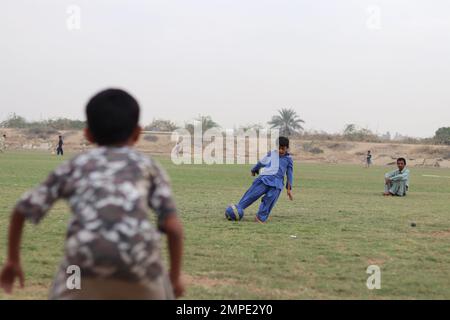 Karatschi Pakistan 2019, ein Kind, das am Sonntagmorgen auf dem Fußballplatz einen Fußball tritt, asiatische Kinder, lokale Sportarten, Fußball in pakistan, Outdoor-aktivitäten Stockfoto