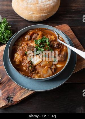 Rindereintopf mit Kohl und Gemüse. Serviert auf rustikalem Holzhintergrund mit hausgemachtem Ciabatta-Brot. Draufsicht Stockfoto