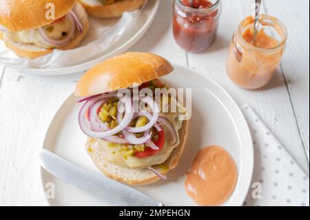 Hausgemachter Hamburger oder Cheeseburger mit roten Zwiebeln, Gurken, Tomaten und Burgersauce auf einem Teller Stockfoto