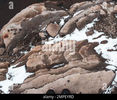 Foto eines felsigen Felsens am Ufer mit dunklem, transparentem Wasser und Schnee Stockfoto