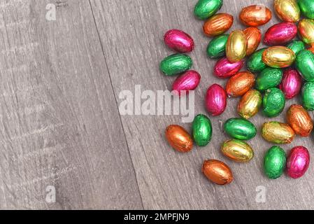 Mehrfarbige Ostereier in rosa, grün, orange und gelb auf einem Haufen oder in einer Gruppe, auf einem grauen weißen Holzhintergrund, in Folie verpackt. Stockfoto